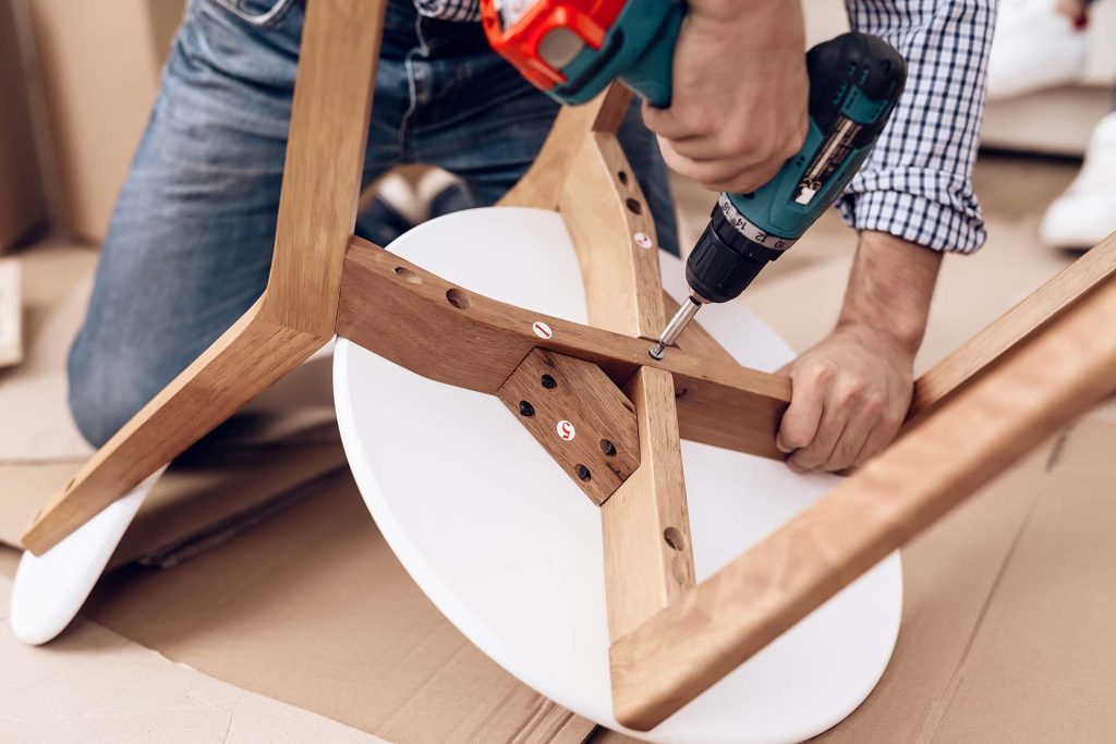 The man handyman is engaged in assembling the chair. The repairman is engaged in mending chair.