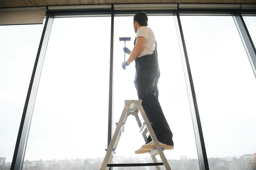 Professional window cleaner using a ladder to clean large commercial windows safely.