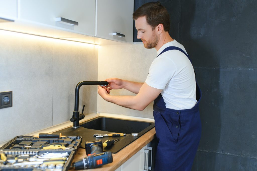 A professional handyman repairing a kitchen faucet with precision tools.