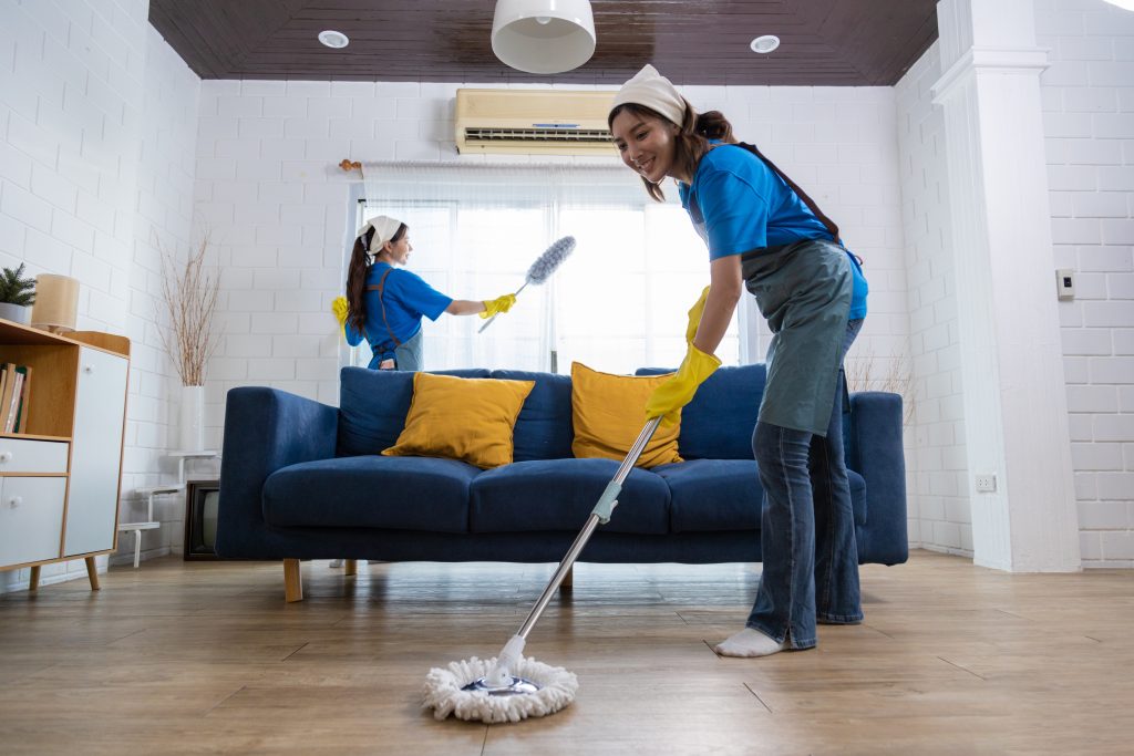 A team of professional cleaners performing deep cleaning in a spacious living room, scrubbing floors and dusting furniture